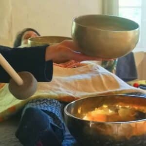 une personne fait sonne un bol chantant, une autre est allongée